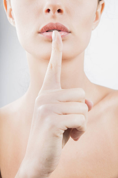 όμορφη νεαρή γυναίκα που κρατώντας το δάχτυλο στα χείλη ως χειρονομία της σιωπής σε λευκό φόντο - Φωτογραφία, εικόνα