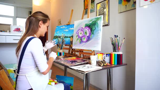 Girl Artist met des gants et prépare de la peinture pour une utilisation dans un studio d'art avec des murs blancs sur lesquels accrochent des photos
. - Séquence, vidéo