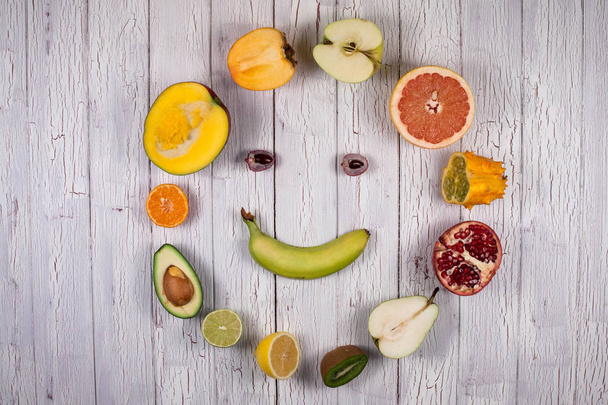 Frutos tropicais maduros frescos em uma tábua de madeira em uma forma de rosto feliz
 - Foto, Imagem