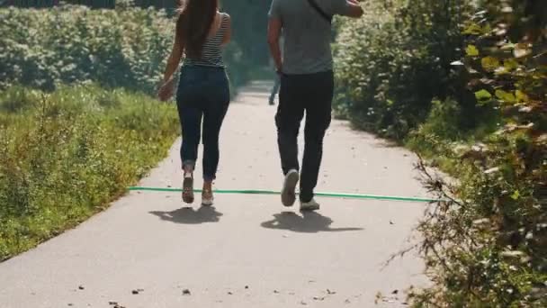 Para odchodzi od kamery wzdłuż drogi asfaltowej w parku w wietrzny dzień - Materiał filmowy, wideo