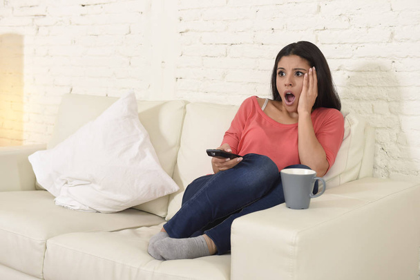  latin woman sitting at home sofa couch in living room watching television scary horror movie - Фото, зображення