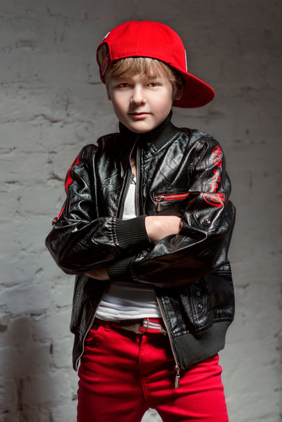 Портрет крутого молодого хип-хоп мальчика в красной шляпе и красных брюках и белой рубашке и черной кожаной куртке на чердаке
 - Фото, изображение