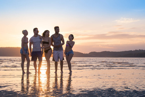 Nuorten ryhmä rannalla auringonlaskun aikaan Kesäloma, Onnelliset hymyilevät ystävät Kävely Seaside
 - Valokuva, kuva