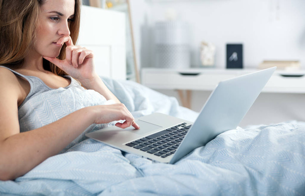 Fiatal lány laptop az ágyban otthon szociális média ellenőrzése - Fotó, kép