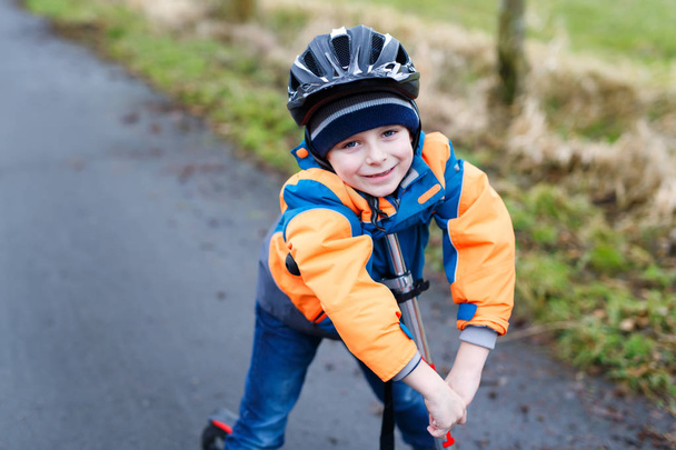 Милый мальчик из детского сада катается на скутере в парке
 - Фото, изображение