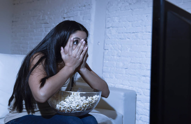Latijnse vrouw in huis banklaag in woonkamer kijken televisie enge horror film of suspense thriller - Foto, afbeelding