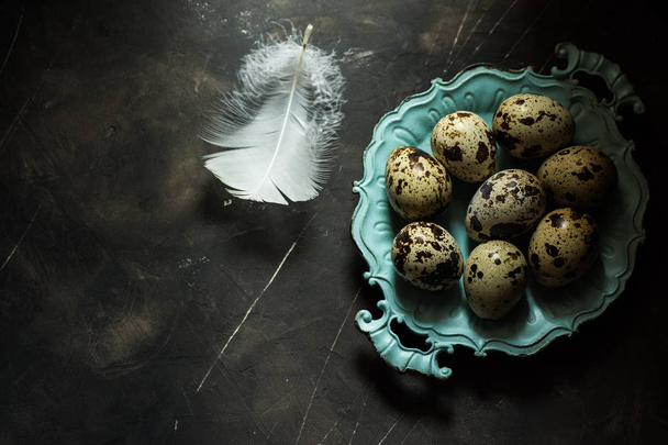 Quail eggs on blue vintage plate,white feather,on black scratched concrete background,Easter concept, minimalistic - Foto, afbeelding