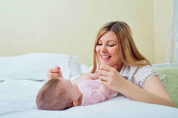 Mother playing with her baby on the bed. Mom smiles to her child - Foto, Imagen