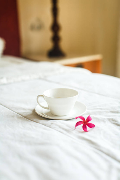 чашка чая и цветок на белой кровати
 - Фото, изображение