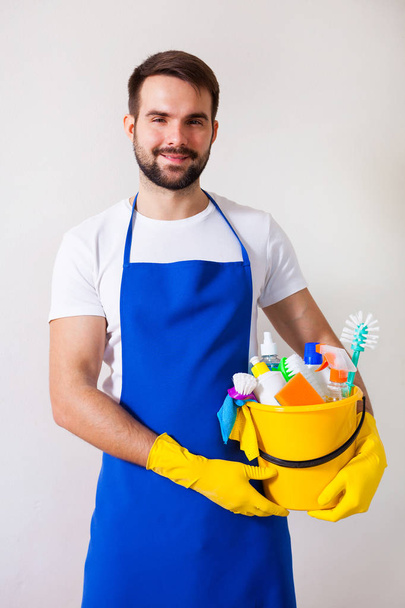 Man holding plastic bucket with bottles and brushes, gloves and  - Foto, Imagen