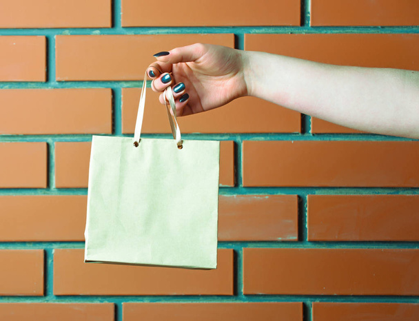 white shopping bag in female hand on brick wall - Foto, afbeelding