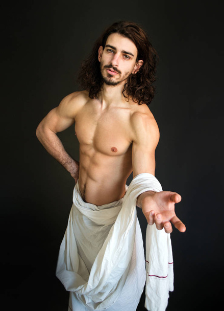 φωτογραφία μυϊκή μισό γυμνός άντρας με σγουρά μαλλιά σε μια λευκή κουρτίνα προσκαλεί - Φωτογραφία, εικόνα