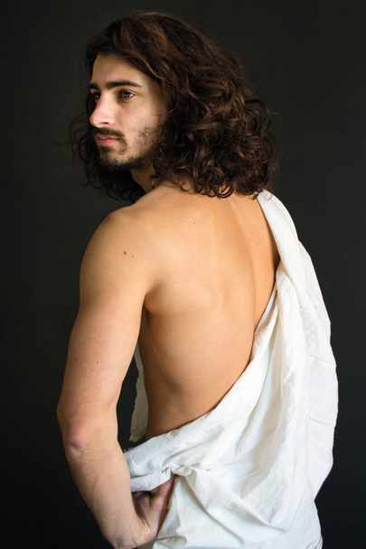 Foto eines Mannes mit lockigem Haar in einem weißen Tuch halb gedreht - Foto, Bild