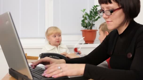 ανύπαντρη μητέρα. δύο μικρά παιδιά παίζεται ενώ η μητέρα τους εργάζεται σκληρά για το φορητό υπολογιστή. κίνηση ζουμ - Πλάνα, βίντεο