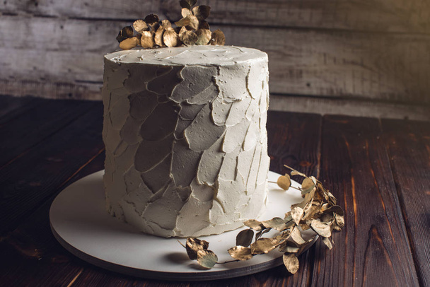 pastel de crema blanca decorada con una rama con hojas de oro
 - Foto, Imagen