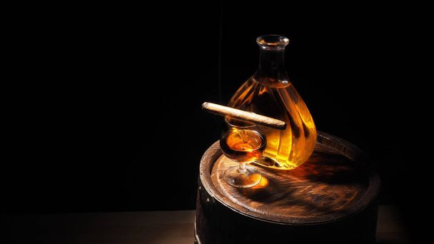 Glass of cognac with barrel on wooden backgroun - Foto, afbeelding