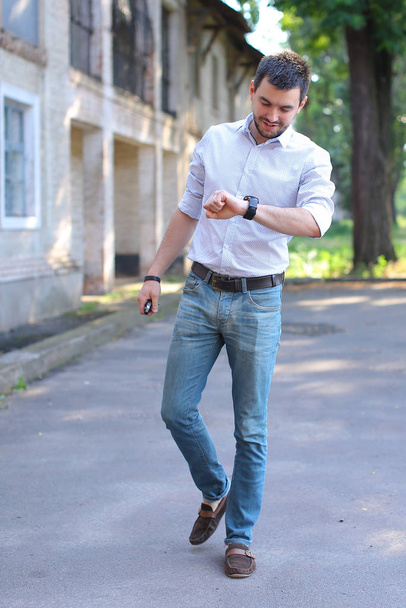 Handsome young man going, walking along road and looks at watch. - 写真・画像