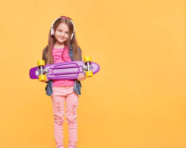 Cute little hipster girl with headphones and skateboard - Zdjęcie, obraz