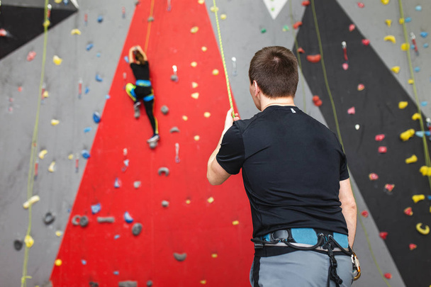 Trainer klettert Laien-Sportler an einer hohen Kletterwand. - Foto, Bild