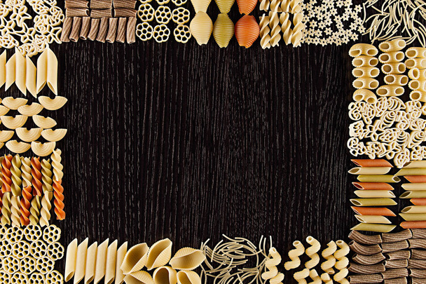 Assortment italian dry pasta on dark brown wooden board with blank copy space as decorative frame background. - Fotografie, Obrázek