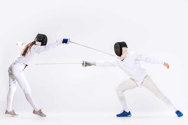 The woman and man wearing fencing suit practicing with sword against gray - Valokuva, kuva