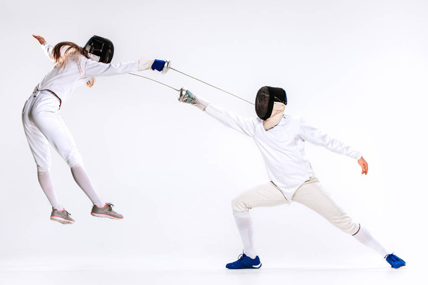 The woman and man wearing fencing suit practicing with sword against gray - Foto, Imagen