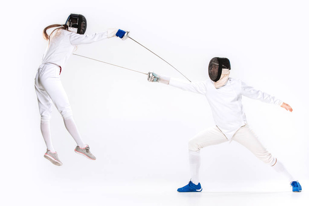 The woman and man wearing fencing suit practicing with sword against gray - Фото, зображення