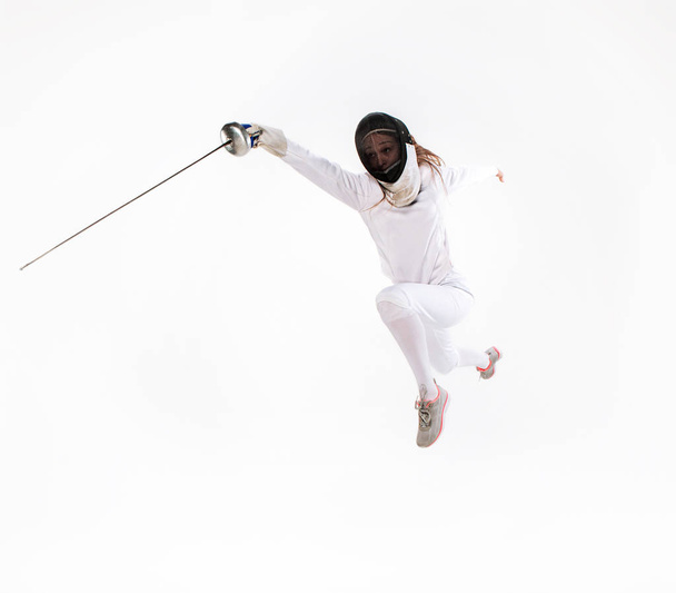 Man wearing fencing suit practicing with sword against gray - Photo, Image