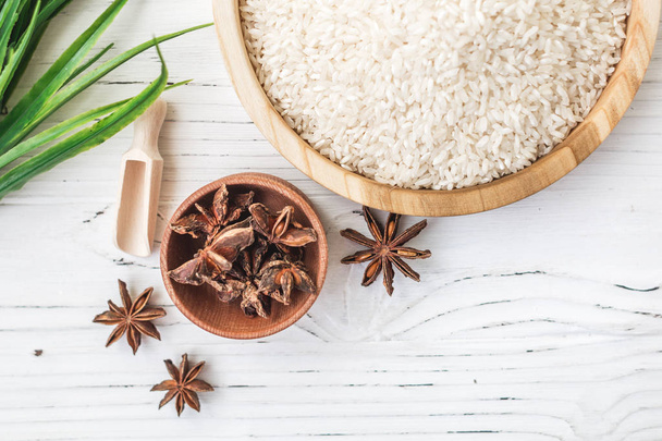 rice in wooden plate and anise on white wooden background. Rice and spices in ecological container. Set for cooking. Set for spa. - Photo, Image