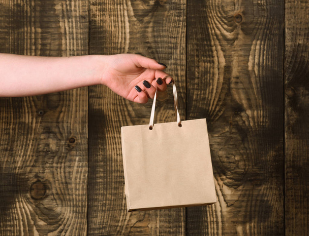 brown grey shopping bag in female hand on wooden background - Zdjęcie, obraz