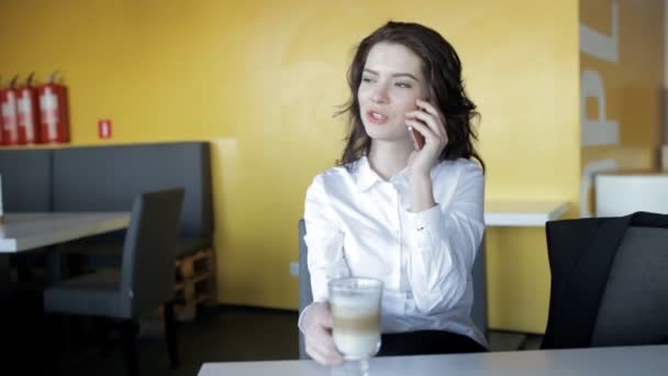 Pretty woman speaking by smartphone and drinking latte in a cafe - Πλάνα, βίντεο