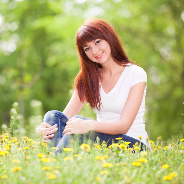 Aranyos nő pihenés a parkban, virágok. Kozmetikai jellegű jelenet színes háttér, a fák és a virágok a tavaszi szezonban. Kültéri életmód. Boldog, mosolygós nő pihenhetnek a zöld fű - Fotó, kép