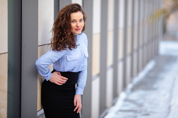 Brunette smiling woman standing near the wall of building, looking forward into camera - Фото, зображення