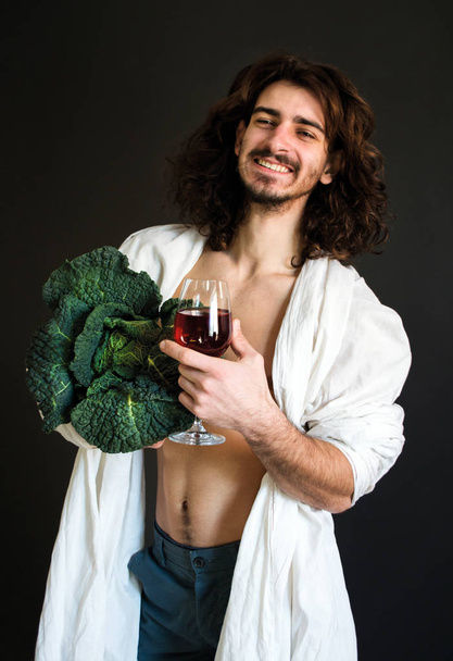 foto man in de witte gordijnen holding van verse groene kool en een glas wijn in zijn handen - Foto, afbeelding