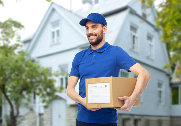 happy delivery man with parcel box over house - Foto, Imagem