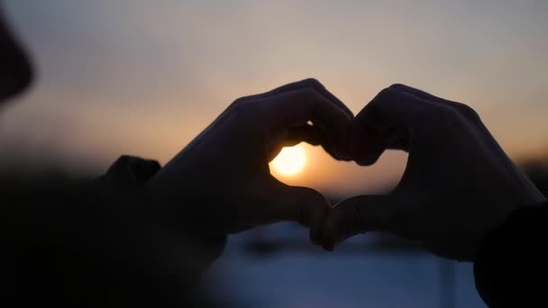 κορίτσι κάνει καρδιά με τα χέρια στον ήλιο. Σιλουέτα χέρι σε σχήμα καρδιάς με μέσα στο ηλιοβασίλεμα. Χειμώνας - Πλάνα, βίντεο