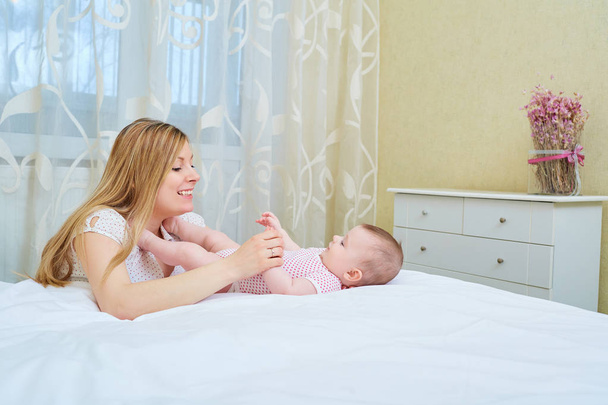 Mother playing with her baby on the bed. Mom smiles to her child - Foto, imagen