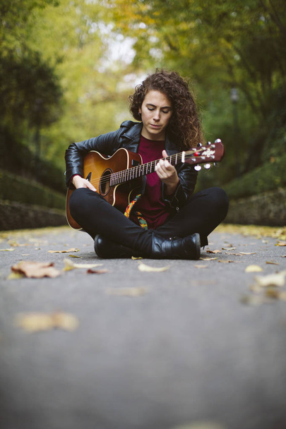Beautiful young woman playing guitar sitting on the forest. - Foto, afbeelding