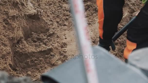 Bouwer in rubber laars graven stapel zand met schoppen in de greppel. Slowmotion - Video