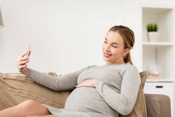 pregnant woman taking smartphone selfie at home - Fotó, kép