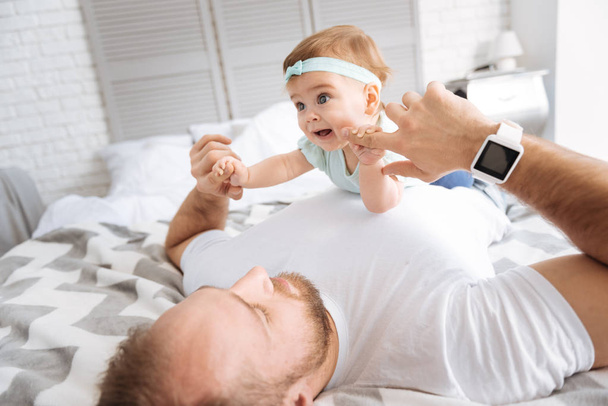 Joyful toddler lying on her father in the bedroom - Foto, afbeelding