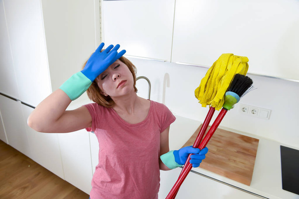Servicefrau in der heimischen Küche in Handschuhen mit Putzbesen und Mopp frustriert - Foto, Bild