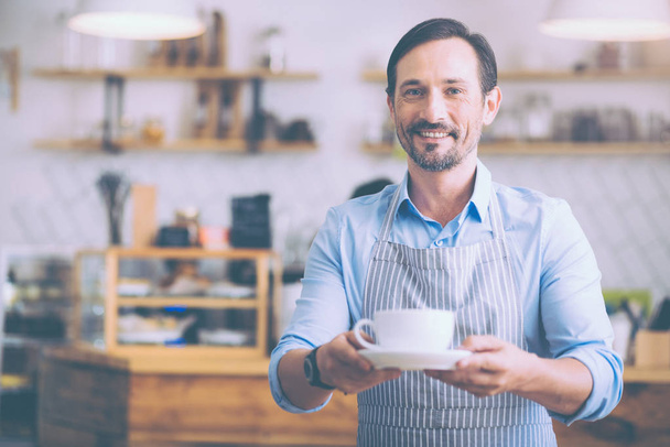 Positive senior waiter holding cup of coffee - Photo, Image