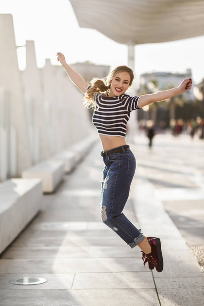Funny blonde woman jumping in urban background.  - Foto, afbeelding