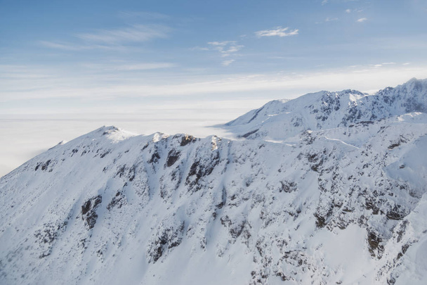 Aerial shot of snowy mountain range on a sunny winter day - Foto, afbeelding