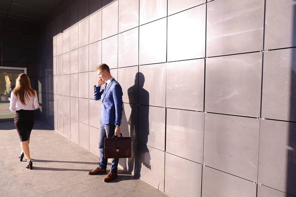 Όμορφος νεαρός άνδρας, επιχειρηματίας, μιλώντας στο τηλέφωνο περνά από την ομορφιά - Φωτογραφία, εικόνα