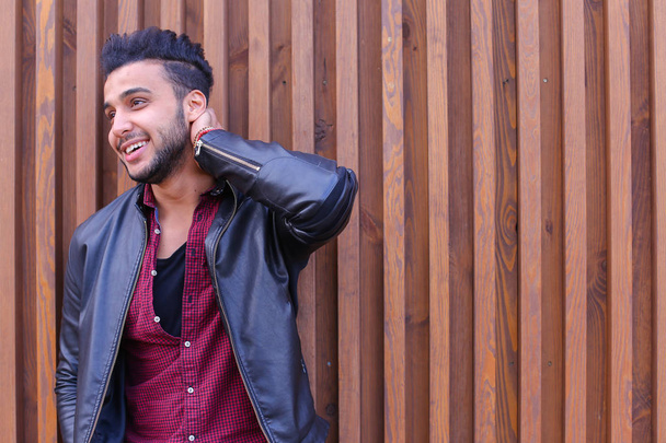 Красивый арабский молодой человек стоит у стены и улыбается, Лауг
 - Фото, изображение