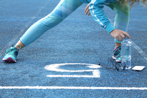 Woman doing exercises on athletic track with mobile phone - Valokuva, kuva