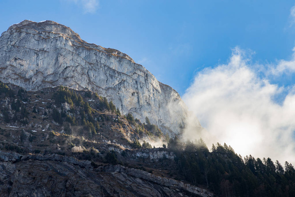 Πρόσωπο απότομων βράχων στο βουνό με τα σύννεφα και τα δέντρα  - Φωτογραφία, εικόνα