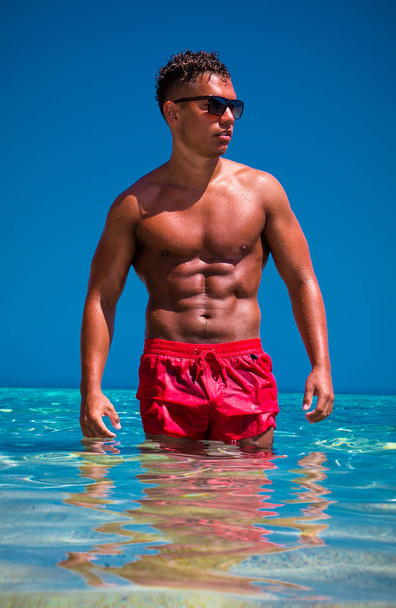 Handsome muscular man wearing sunglasses in sea water - Foto, afbeelding